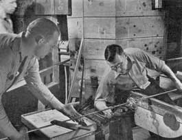 Attaching the Pontil Rod: Stem and foot having been formed and worked to the desired shape, the next step is to attach the pontil rod to the base. The gaffer is seated at his bench and his servitor, or helper, is seen at the left holding the pontil rod in position as it is made fast to the foot.