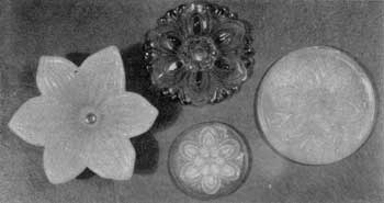 Four Sandwich Tieback Rosettes: Except for the one in the upper center, all are of opalescent glass. That at the lower left is a copy in glass of the clematis flower. The others are all of the same conventionalized floral design but show minor variations.