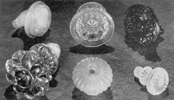 Fragments from Sandwich: Upper row, left to right: Conventionalized floral designs in opalescent, canary-yellow, and dark-blue glass. Lower row: Large rosette knob with glass screw shank (not found at Sandwich but attributed to it), broken, ribbed mushroom knob, and small knob with screcw-threaded shank. The last two are of clear glass that has become frosted from being buried in the ground.